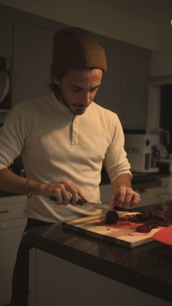 Chef Bruno Di Benedetto slicing roasted beetroot on a wooden board in a warmly lit kitchen