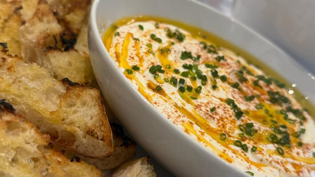 Bowl of whipped hummus with olive oil, paprika and torn sourdough