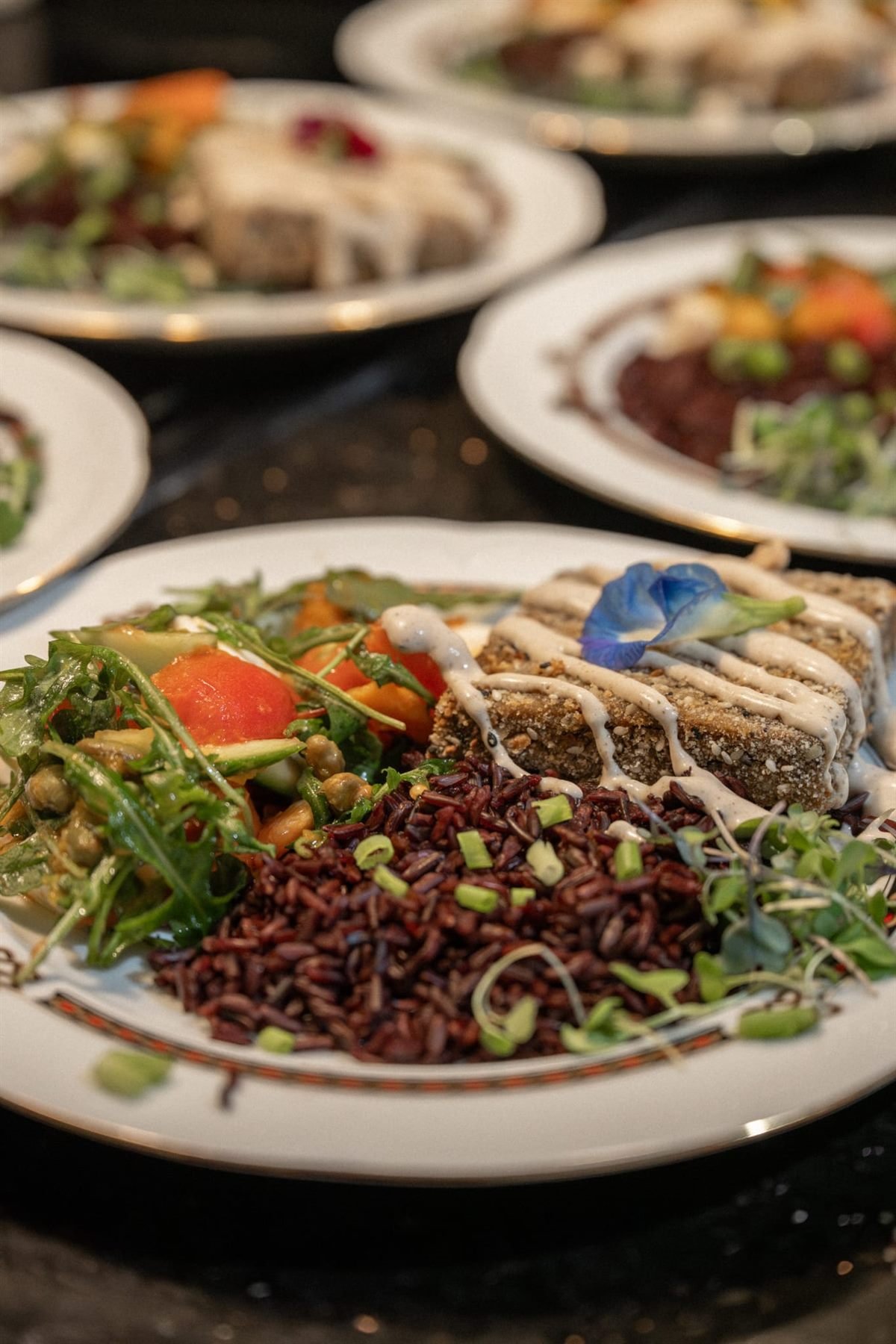 Plated black rice course with herb-crusted fish and edible flowers served at a private chef dinner
